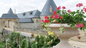 A stone building with conical roofs, a large stone planter with red flowers, and a stone wall in the foreground. - Large gîte with indoor pool and sauna (Charbogne)