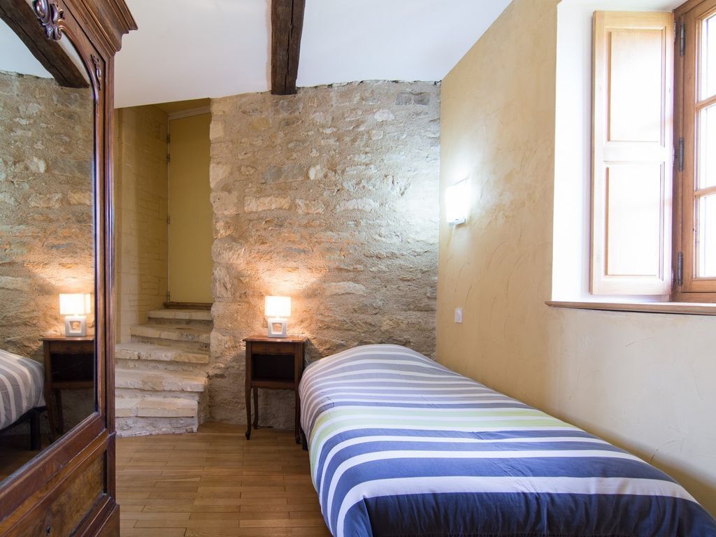 A bedroom with a stone wall, a wooden bed, a window, and a staircase.