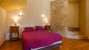 A bedroom with a bed, two bedside tables, a stone wall, and a staircase. - Large gîte with indoor pool and sauna (Charbogne)