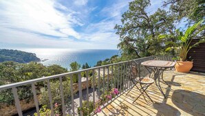 Una terraza con una mesa y sillas, con vistas a un paisaje costero con árboles y el mar.