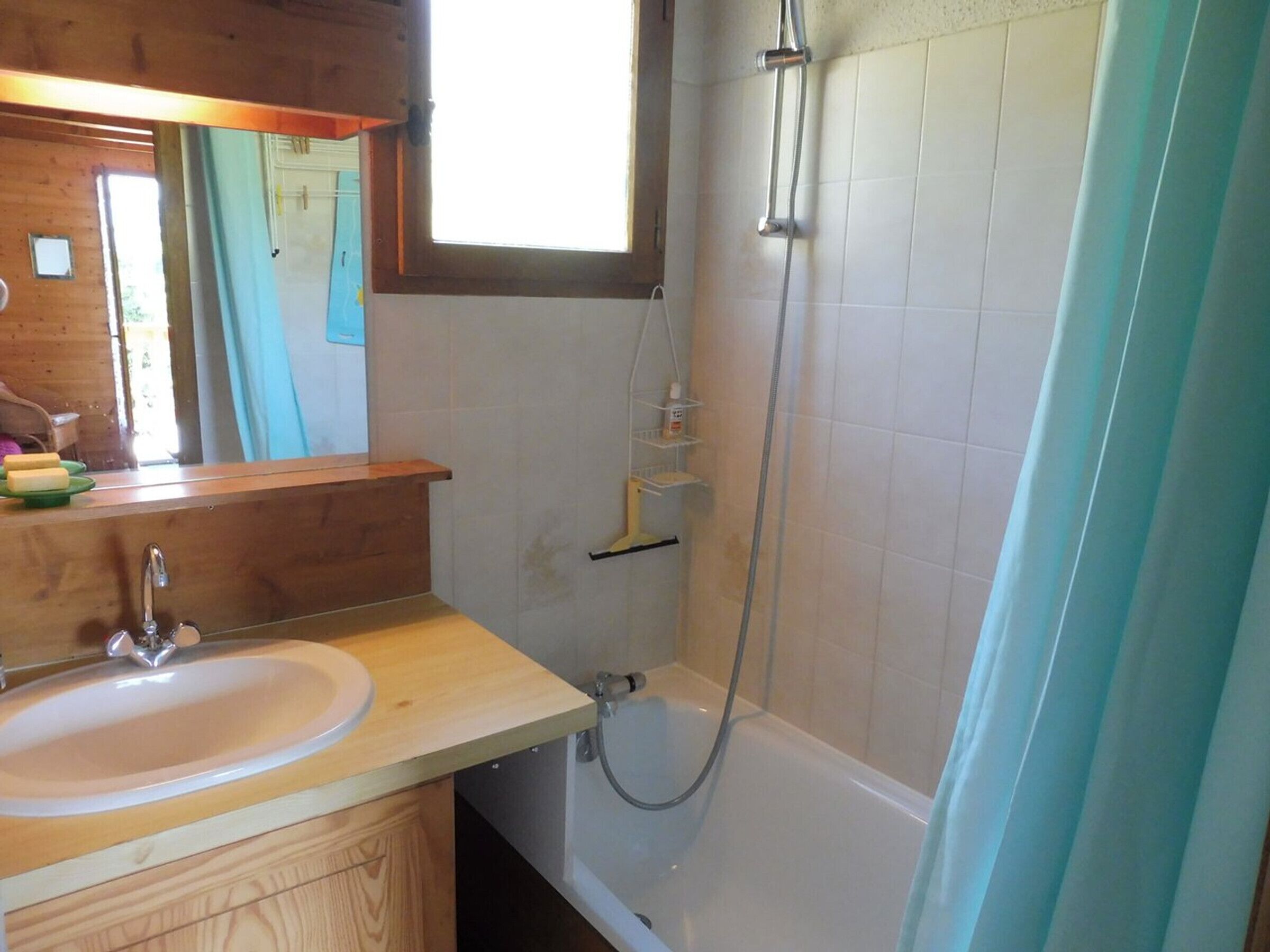 Ein Badezimmer mit einem Holzkosmetikschrank, einem Waschbecken, einem Spiegel, einer Dusche und einem Fenster.