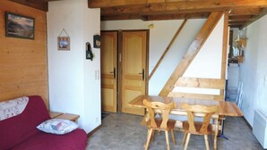 A cozy room with a wooden ceiling, a wooden dining table with chairs, a red sofa with a patterned cushion, and a door leading to another room. - Duplex for 6 with Garage, Near Slopes in Crest-Voland (Crest-Voland)