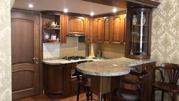 A kitchen with wooden cabinets, a granite countertop, a gas stove, and a bar area with stools. - Duplex apartment in the historical center of Odessa (Odessa)