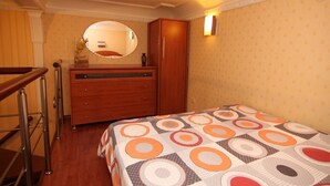 A bedroom with a bed, a wooden dresser, a mirror, and a wall-mounted light. - Duplex apartment in the historical center of Odessa (Odessa)