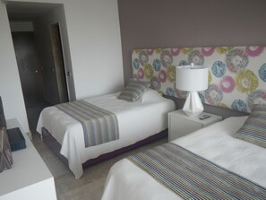 Une chambre d’hôtel avec deux lits, une table de chevet avec une lampe, une porte et un mur orné d’un motif floral.
