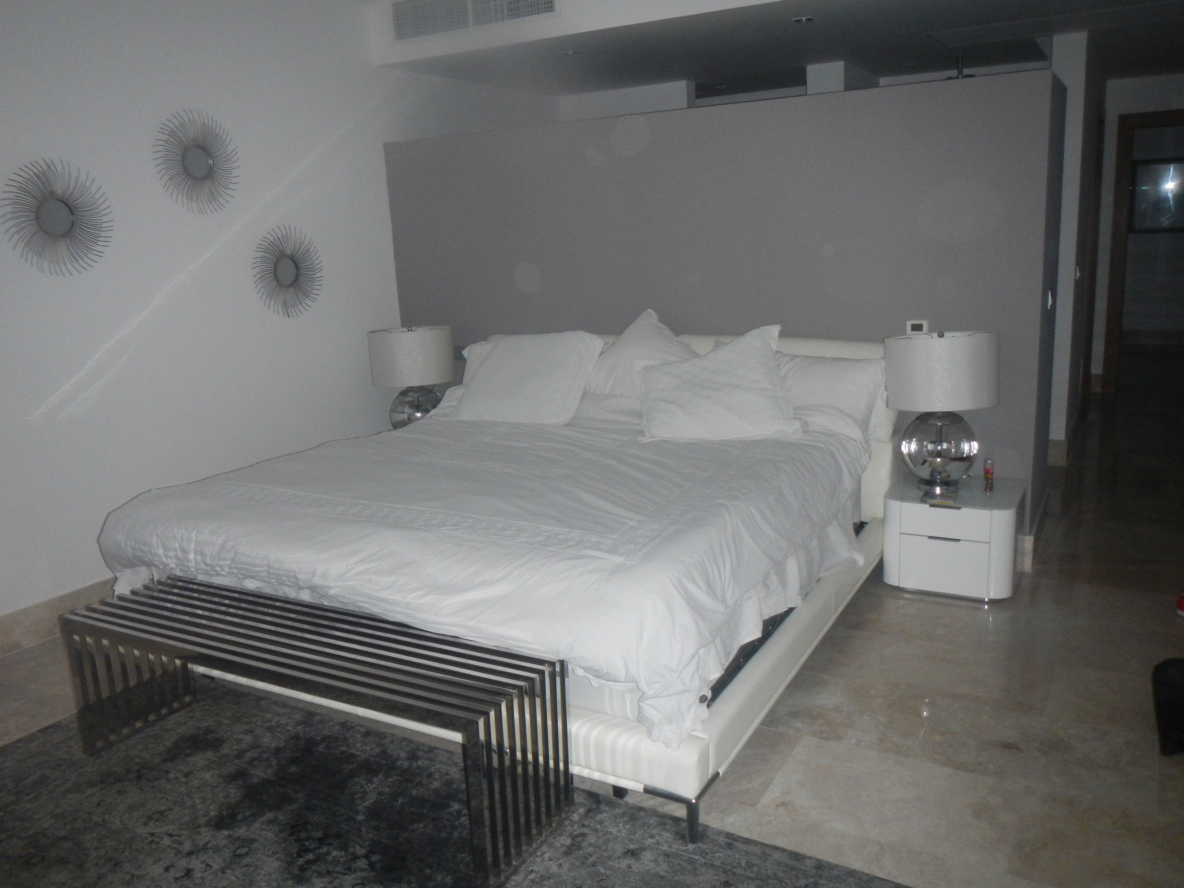 Een moderne slaapkamer met een groot bed, een nachtkastje, een lamp en decoratieve wandlampen.