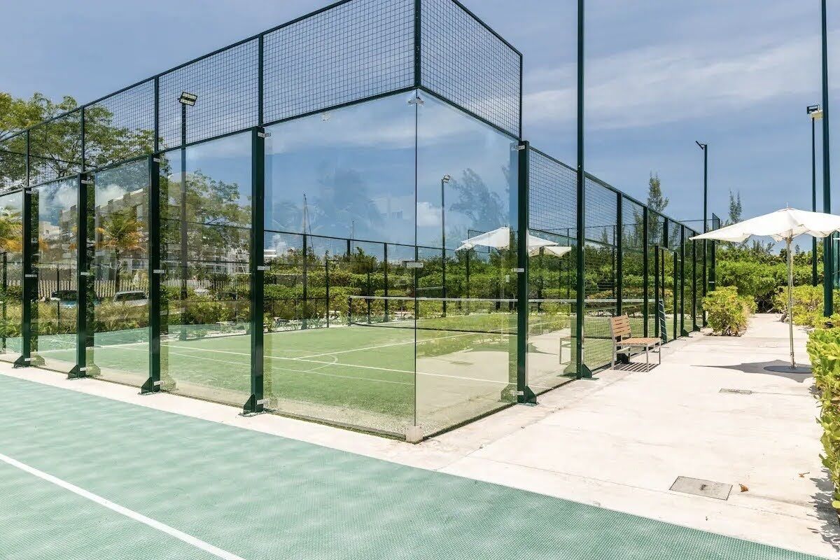 A tennis court with a glass enclosure, benches, and a pathway.