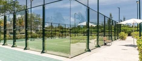 A tennis court with a glass enclosure, benches, and a pathway.