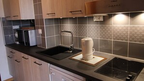 Een moderne keuken met houten kastjes, een zwart aanrecht, een Bosch vaatwasser, een spoelbak en een koffieapparaat.