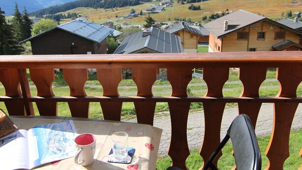 Een balkon met een tafel, een boek en een mok.