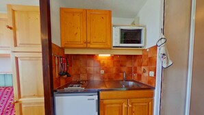 Una cucina compatta con mobili in legno, un forno a microonde, un lavello e un frigorifero.