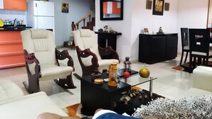 A living room with a sofa, chairs, a coffee table with decorative items, a kitchen area with a refrigerator, and a staircase. - Cabin With Ocean and Forest Views (Tubará)
