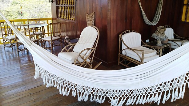A hammock chair set on a wooden deck with wicker furniture and a decorative wall panel. - Cabin With Ocean and Forest Views (Tubará)