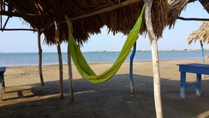 A hammock under a thatched roof, a blue bench, and a sandy beach with a calm sea in the background. - Cabin With Ocean and Forest Views (Tubará)
