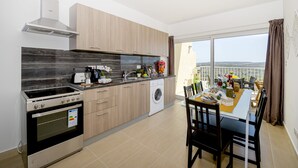 Una cocina moderna con estufa, horno y lavadora, un comedor con mesa lista para cuatro personas, y un amplio ventanal con vista a la ciudad.