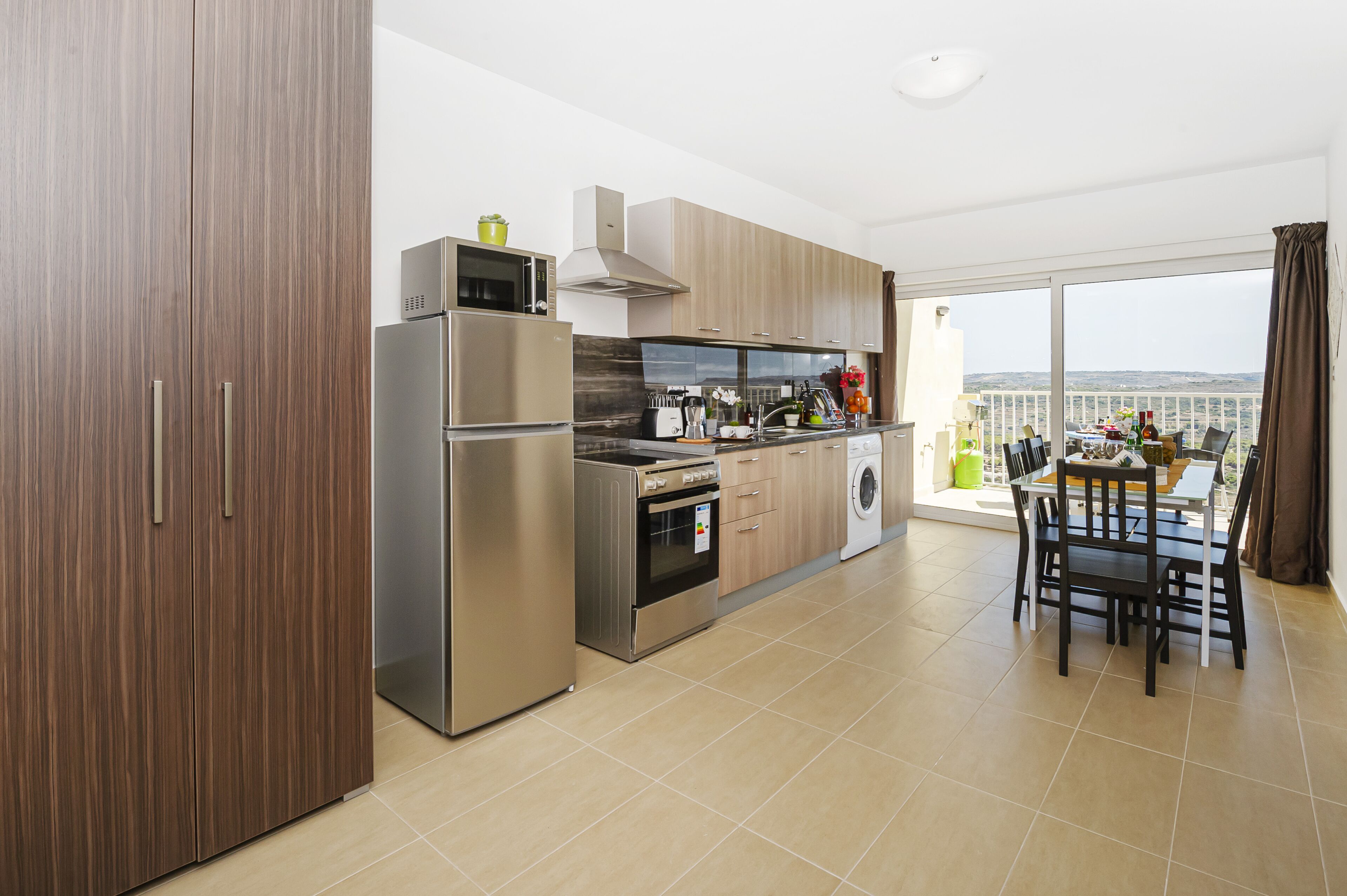 A modern kitchen with stainless steel appliances, wooden cabinets, and a dining area with a view.