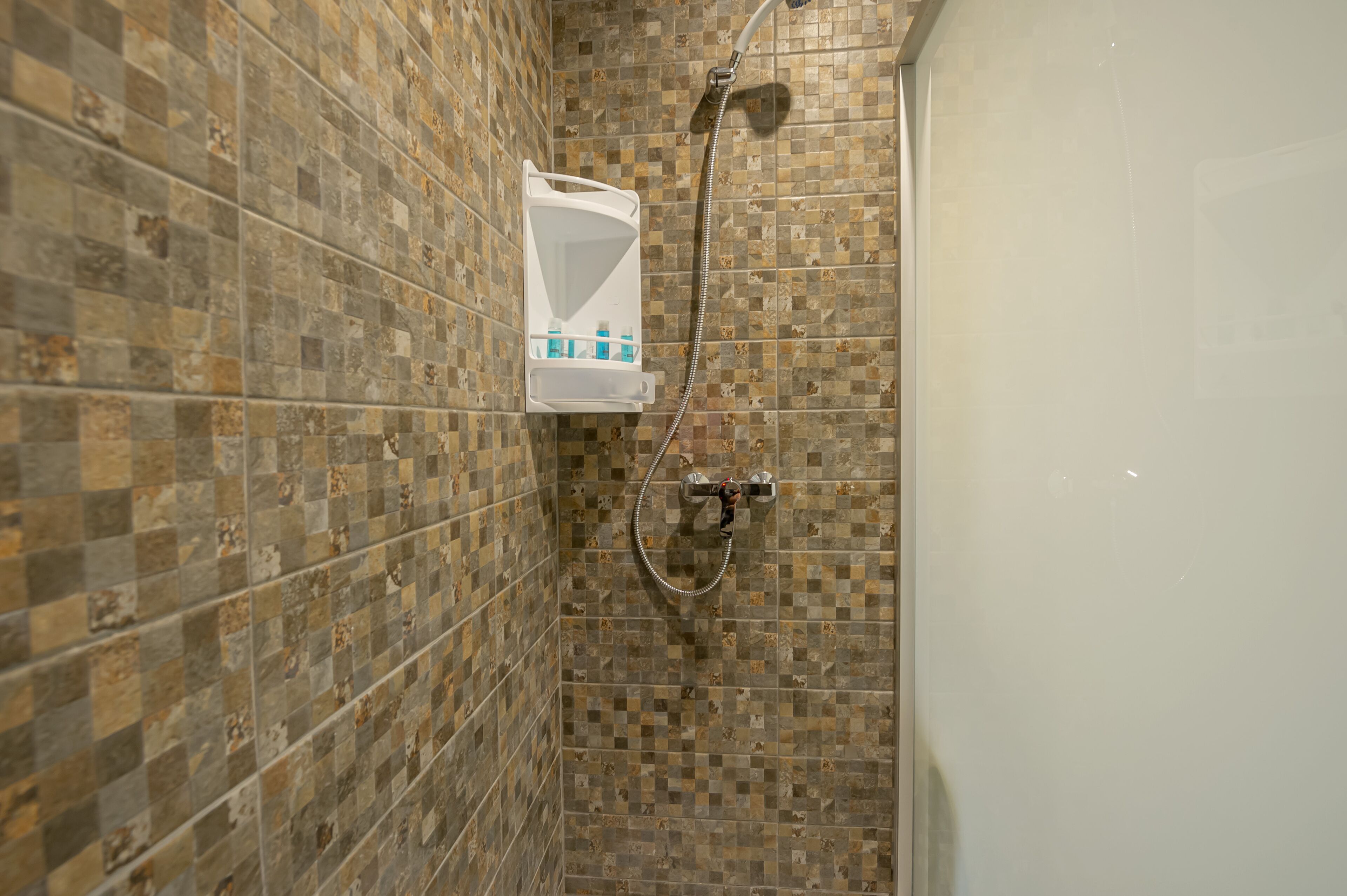 A bathroom with mosaic tile walls and a shower with a handheld showerhead.