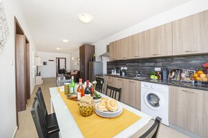 Una cocina moderna con armarios de madera, lavadora integrada y un comedor con una mesa para dos.