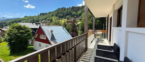 Un balcon donnant sur une maison rouge et une colline boisée.