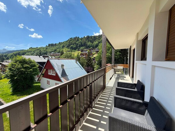 A balcony with a view of a red house and a forested hill.