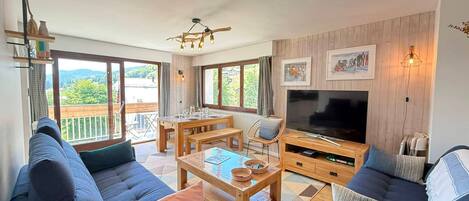 Sala de estar con sofá, mesa de centro, televisor y comedor, con vista a un balcón.