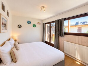 A bedroom with a large bed, a window with curtains, a radiator, and wall decorations.
