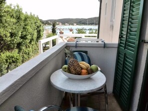 Un balcón con una mesa que sostiene un cuenco de fruta, una silla y vistas a un puerto deportivo y colinas.