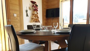 A dining area with a round table set for four, wooden chairs, and a Christmas tree decoration. - Quiet 3-room Apartment Les Gets, incl. garage (Les Gets)