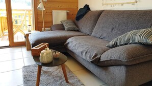 A cozy living room with a grey sofa, a small round table with a teapot and cups, a wooden floor, and a wooden ceiling. - Quiet 3-room Apartment Les Gets, incl. garage (Les Gets)