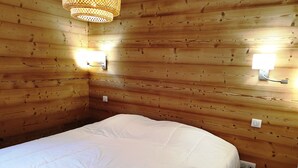 A wooden-paneled room with a bed, two wall-mounted lights, and a small round table with a tissue box. - Quiet 3-room Apartment Les Gets, incl. garage (Les Gets)