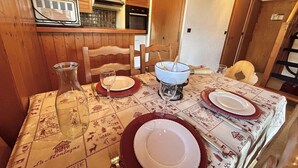 A dining table set with plates, glasses, and a bowl, in a room with wooden cabinets and a kitchen area. - Charming 3-Room Apartment with Mezzanine, 1km from Ski Lifts - Megève (Megève)