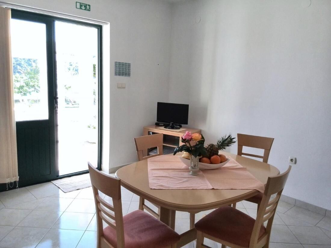 A dining area with a round table, four chairs, a small TV, and a bowl of fruit and flowers on the table.