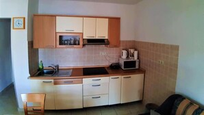 A small kitchen with wooden cabinets, a microwave, and a sink. - Guesthouse Raffaello (Rab)