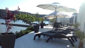 A terrace with lounge chairs and umbrellas overlooking a body of water. - Guesthouse Raffaello (Rab)