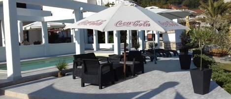 Outdoor seating with umbrellas, a pool, and a building with a white facade.