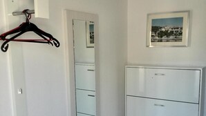 Una habitación con un armario blanco, un espejo, un cuadro en la pared y un perchero.