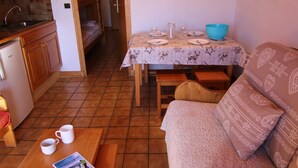 Un espace de vie compact comprenant un coin cuisine, une table à manger pour quatre personnes, un canapé et une petite table avec deux tasses et un magazine.