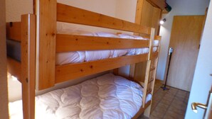Un lit superposé avec une tête de lit et un pied de lit en bois, une literie blanche et un sol carrelé.