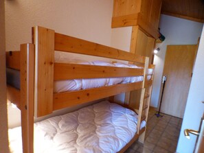 A bunk bed with wooden headboard and footboard, white bedding, and a tiled floor.