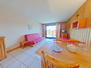 A cozy living room with a sofa, a dining table with chairs, a TV, and a wooden cabinet.