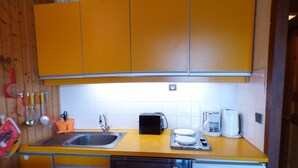 Una cocina compacta con gabinetes amarillos, un lavamanos, lavavajillas, cafetera y tostadora.