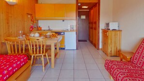 Una cocina compacta con armarios de madera, una mesa de comedor con sillas, un refrigerador pequeño y un microondas.