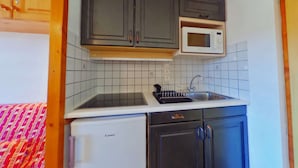 Une petite cuisine équipée avec des meubles de couleur sombre, un plan de travail blanc, un four à micro-ondes encastré, un évier et un petit réfrigérateur.