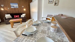 A dining area with a table set for four, surrounded by white chairs. A wooden bench and a sofa are visible in the background. - Cozy Studio with Balcony, Near Ski Lift, Pool & Tennis, Megève - Sleeps 4 (Megève)