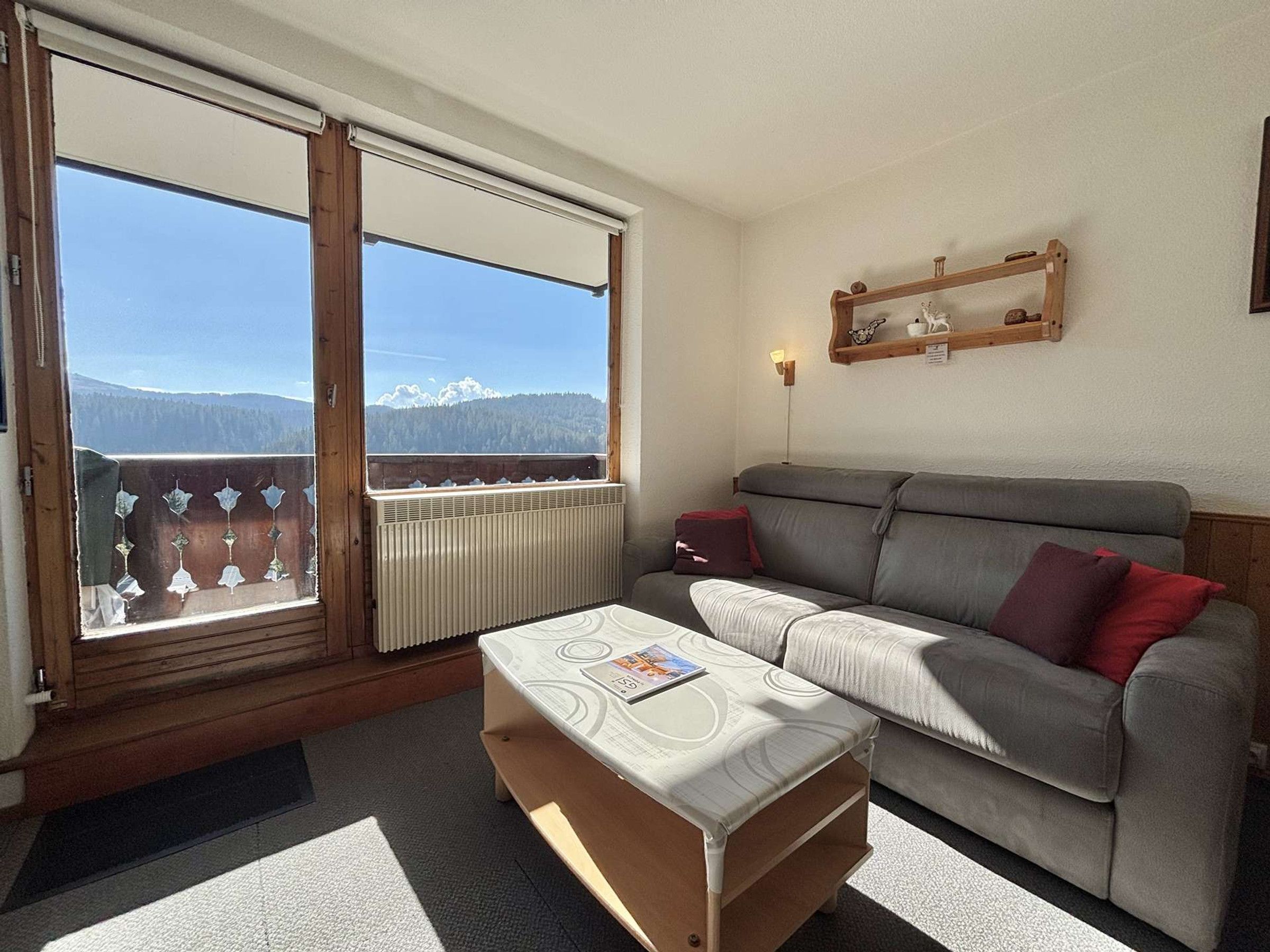 A living room with a sofa, a small table, and a view of a mountainous landscape through a large window.
