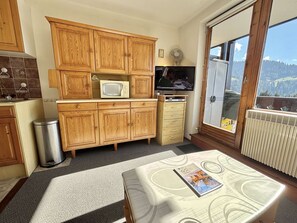 A compact kitchen with wooden cabinets, a microwave, a television, and a window with a view of a mountainous landscape. - Functional studio cabin for 6 at the foot of the slopes - Parking included (Notre-Dame-de-Bellecombe)