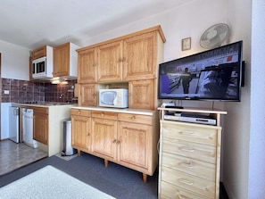 A compact kitchen with wooden cabinets, a microwave, a dishwasher, and a flat-screen TV mounted on the wall. - Functional studio cabin for 6 at the foot of the slopes - Parking included (Notre-Dame-de-Bellecombe)