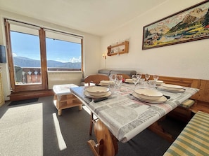 A dining area with a table set for six, a sofa, a window with a mountain view, and a painting on the wall. - Functional studio cabin for 6 at the foot of the slopes - Parking included (Notre-Dame-de-Bellecombe)