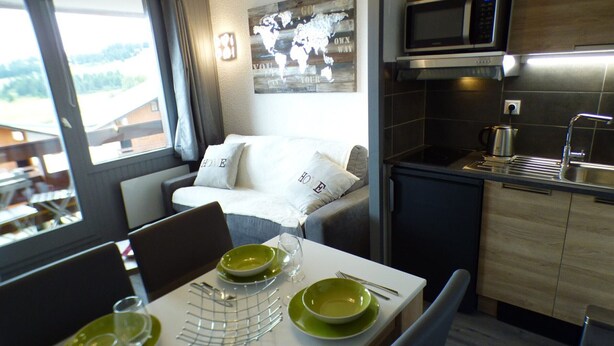 A modern hotel room with a dining area, kitchenette, and a large window with curtains. - Cozy studio Les Saisies 4 people (Les Saisies)