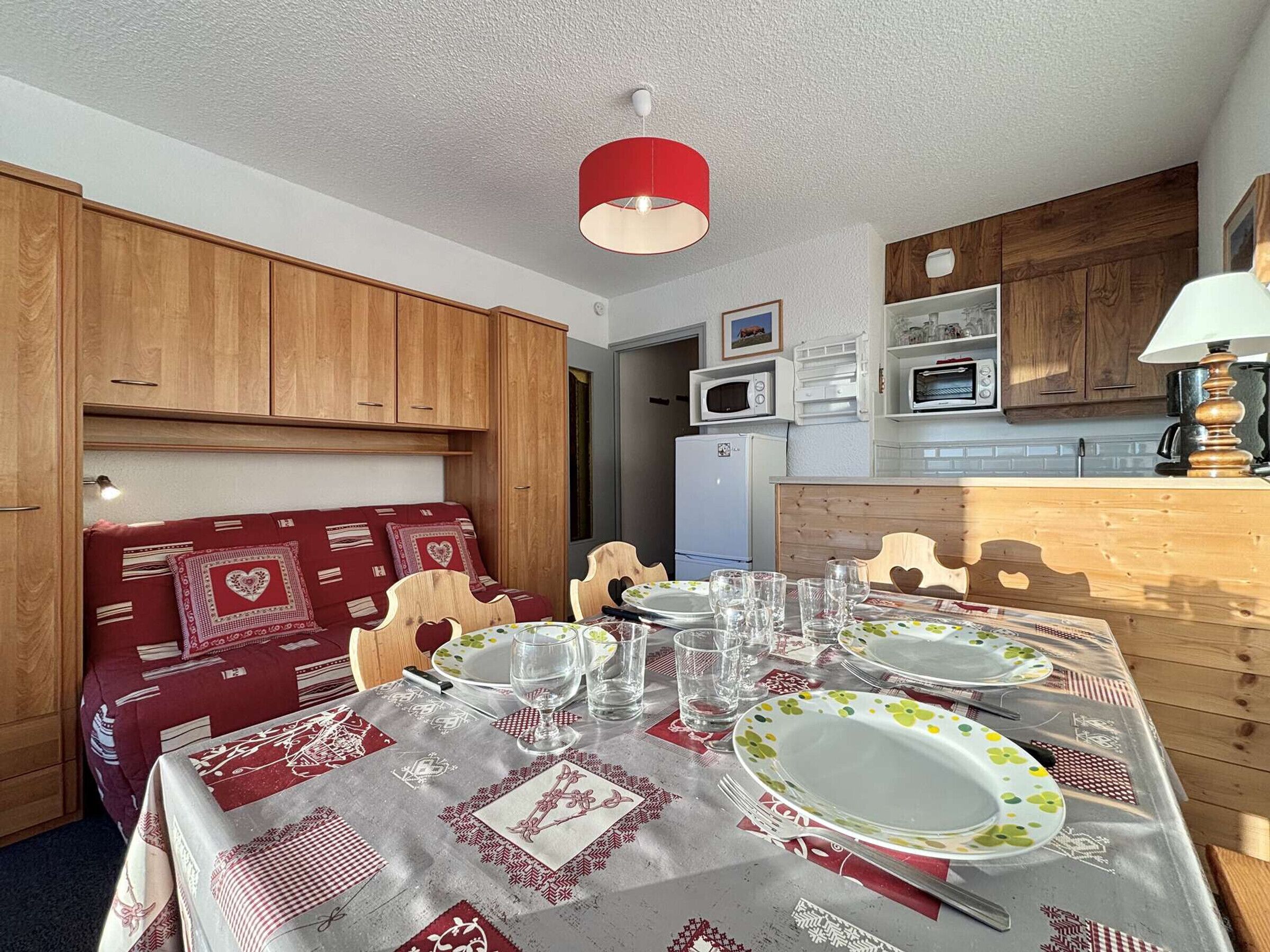 A dining area with a table set for four, wooden cabinets, a microwave, and a refrigerator.
